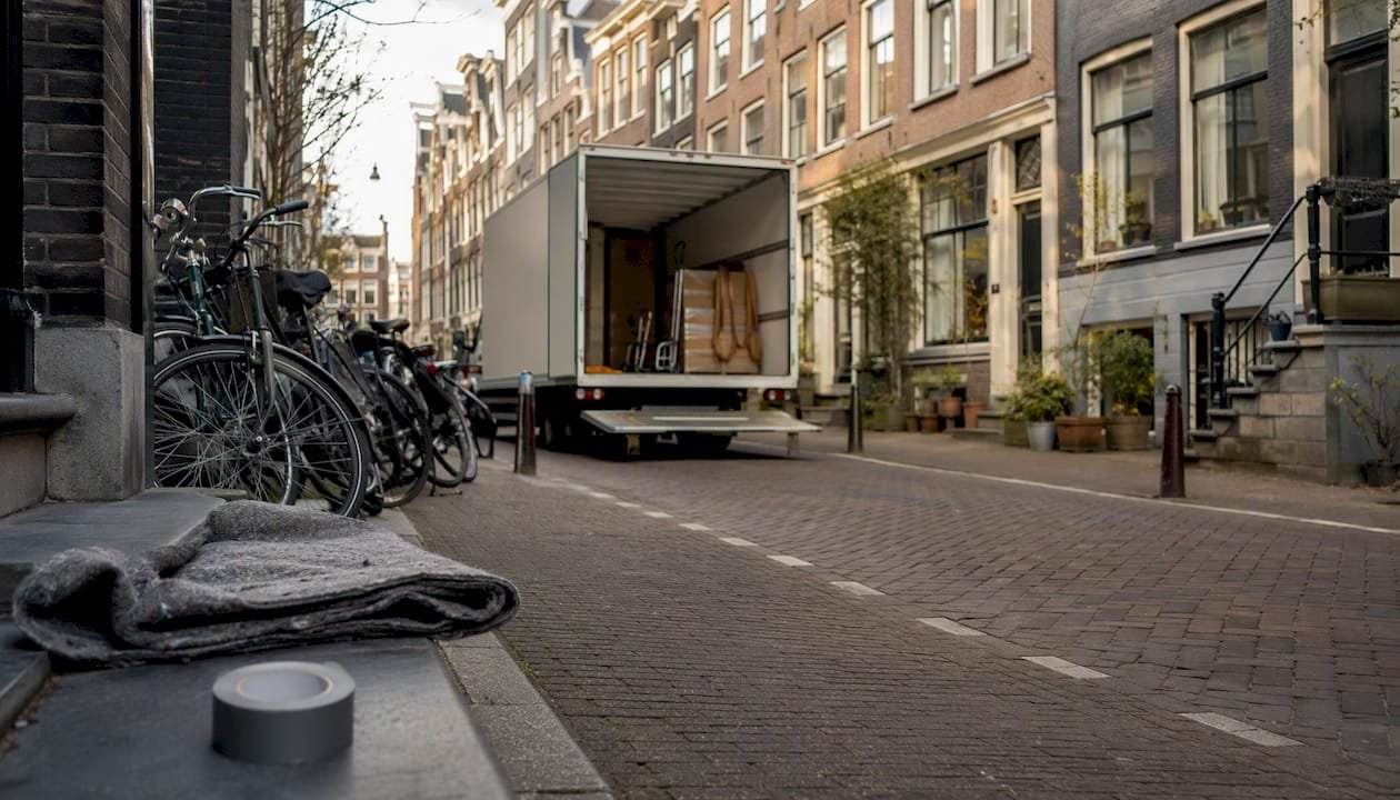 Een smal Amsterdams straatje waar een grote verhuiswagen staat geparkeerd.