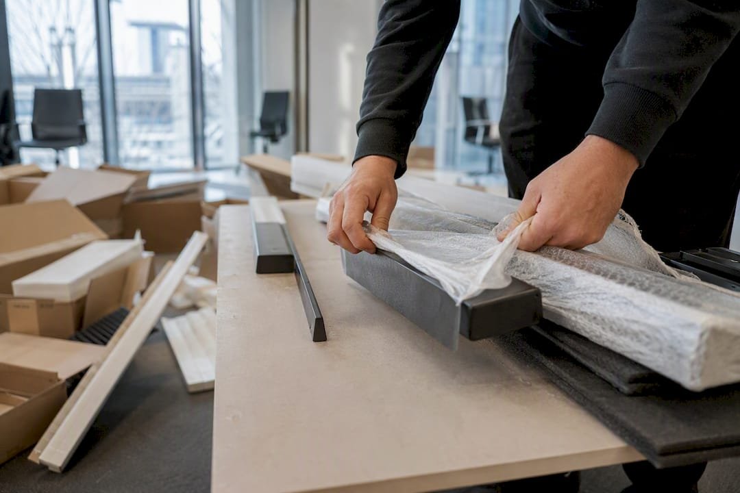 Handen halen zorgvuldig de onderdelen van nieuw kantoormeubilair uit de verpakking.