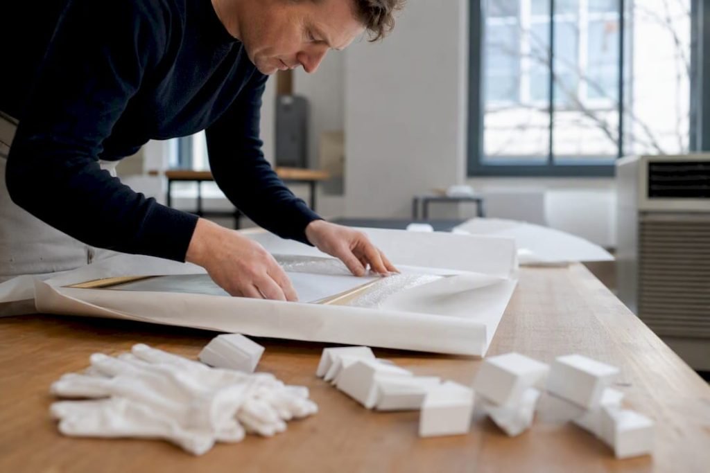 Een kunstverzorger pakt een schilderij zorgvuldig in met beschermende materialen.